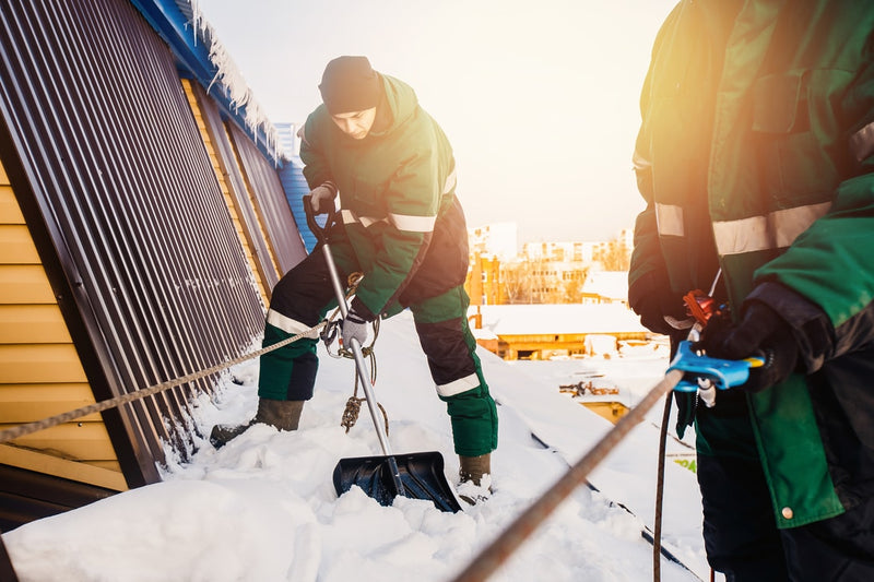 Foto von zwei Arbeitern, welche im Winter ein Dach vom Schnee befreien