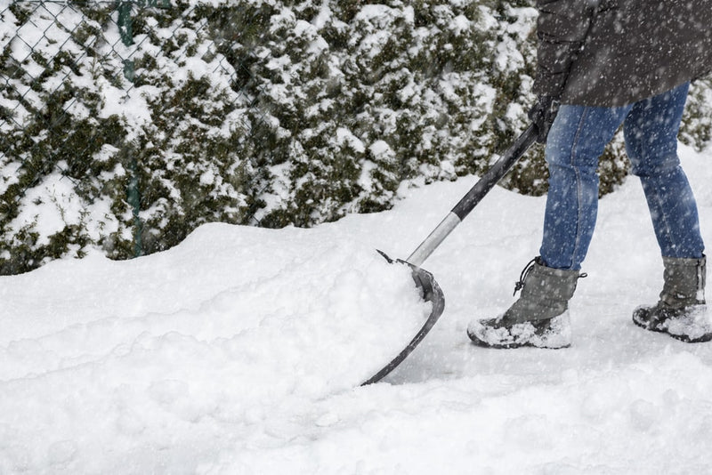 Foto einer Person welche im Winter bei Schneefall am Schneeschaufeln ist